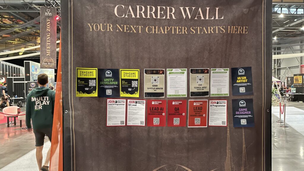 Messewand mit der Aufschrift "Carrer Wall, your next chapter starts here". Darunter zwei Reihen bunter Stellenanzeigen verschiedener Spielestudios mit QR-Codes. Links geht eine Person in grünem Kapuzenpullover mit der Aufschrift "Multiplayer" vorbei.